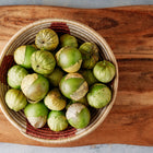 Purple de Milpa tomatillos with papery husks in a woven basket on a wooden cutting board.