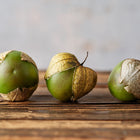 Three Purple Tomatillo fruits with papery husks resting on a rustic wooden surface.
