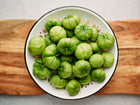 Freshly harvested Verde tomatillos in a white enamel colander set on a wooden cutting board.
