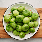 Freshly harvested Verde tomatillos in a white enamel colander set on a wooden cutting board.