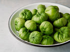Freshly harvested Verde tomatillos in papery husks piled in a white enamel colander.