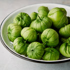 Freshly harvested Verde tomatillos in papery husks piled in a white enamel colander.