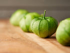 Fresh green Verde tomatillos in papery husks arranged in a row on a wooden surface.