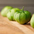 Fresh green Verde tomatillos in papery husks arranged in a row on a wooden surface.