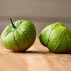 Two fresh Verde tomatillos with papery green husks resting on a wooden surface.
