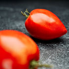 Two red Amish Paste tomatoes with an oxheart shape resting on a dark, textured surface.