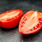Two halves of a bright red Amish Paste tomato showing meaty, low-seed flesh on a dark stone surface.