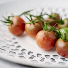 Dusky purple-brown Black Cherry tomatoes on a vine resting in a white decorative bowl.