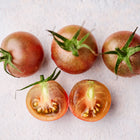Three whole and two halved Black Cherry tomatoes with dusky purple-brown skin and juicy flesh on a light surface.