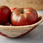 Mahogany-red Black Krim tomatoes with green shoulders resting in a woven decorative bowl.