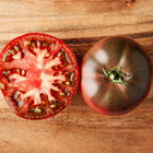 Whole and sliced Black Krim tomato showing mahogany-red flesh and dark skin on a wooden surface.