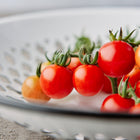 A cluster of bright red Chadwick Cherry tomatoes with green stems resting in a white decorative bowl.