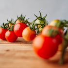 A cluster of bright red, round Chadwick Cherry tomatoes on a vine resting on a wooden surface.