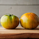 Two ripe Cherokee Green tomatoes with chartreuse and amber skin on a wooden surface.