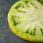 A cross-section slice of a chartreuse Cherokee Green tomato showing dense flesh and seeds on a dark surface.