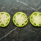 Three slices of Cherokee Green tomato showing chartreuse flesh and seeds on a dark marble surface.