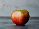 A single Cherokee Purple tomato with dusky rose-purple skin and dark green shoulders on a dark surface.