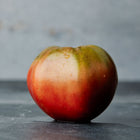 A single Cherokee Purple tomato with dusky rose-purple skin and dark green shoulders on a dark surface.