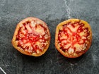 Two slices of a Cherokee Purple tomato showing deep red, juicy flesh on a dark marble surface.