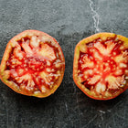Two slices of a Cherokee Purple tomato showing deep red, juicy flesh on a dark marble surface.