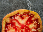 Cross-section of a Cherokee Purple tomato showing red, juicy flesh and green-tinted skin on a dark stone background.