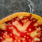 Cross-section of a Cherokee Purple tomato showing red, juicy flesh and green-tinted skin on a dark stone background.