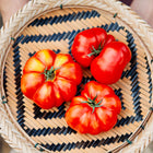 Three red, ribbed Costoluto Genovese tomatoes in a woven bamboo basket with a black and tan geometric pattern.