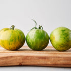 Three Green Zebra tomatoes with lime-yellow stripes sitting on a wooden cutting board.