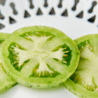 Three bright green slices of Green Zebra tomato showing internal seeds and flesh on a white patterned plate.
