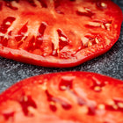Two thick, juicy slices of pink-red Mortgage Lifter tomato resting on a dark, textured surface.