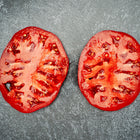 Two thick, juicy slices of a red Mortgage Lifter tomato showing meaty interior texture on a dark gray surface.