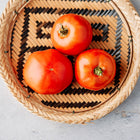 Three red Moskvich tomatoes resting in a round, woven wicker basket with a geometric black and tan pattern.