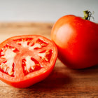 One whole and one sliced Moskvich tomato showing red flesh and seeds on a wooden cutting board.
