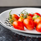 Principe Borghese tomatoes with green stems arranged in a white decorative bowl on a dark surface.