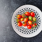 Principe Borghese tomatoes on the vine in a white decorative bowl with a black pattern on a dark textured surface.