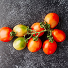 A cluster of Principe Borghese tomatoes with red and green skin on a dark, textured surface.