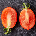 Two halves of a Principe Borghese tomato showing red, meaty interiors on a dark, textured surface.