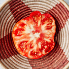 Sliced Red Brandywine tomato showing meaty red flesh inside a patterned woven bowl.