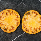 Two thick, golden-yellow slices of Yellow Brandywine tomato resting on a dark, marbled surface.