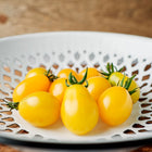 Fresh Yellow Pear tomatoes in a white decorative bowl on a wooden surface.