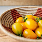 Yellow Pear tomatoes in a woven basket with red and tan patterns on a wooden surface.