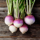 Freshly harvested Purple Top White Globe turnips with green stems arranged on a dark, rustic wooden surface.