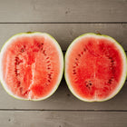Two halves of a Crimson Sweet watermelon with bright red flesh and dark seeds on a grey wooden surface.