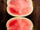 Two halves of a sliced Moon and Stars watermelon showing bright red flesh and dark seeds on a rustic wooden surface.