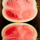 Two halves of a sliced Moon and Stars watermelon showing bright red flesh and dark seeds on a rustic wooden surface.