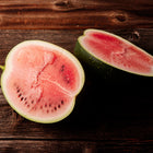 Two halves of a Moon and Stars watermelon showing bright red flesh and dark seeds on a rustic wooden surface.