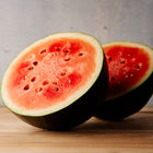 Two halves of a Sugar Baby watermelon showing bright red flesh and dark green rinds on a wooden surface.