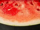 Close-up of a juicy, bright red Sugar Baby watermelon slice with dark seeds and a light green rind.