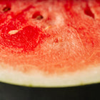 Close-up of a juicy, bright red Sugar Baby watermelon slice with dark seeds and a light green rind.