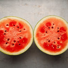 Two halves of a Sugar Baby watermelon showing bright red flesh and dark seeds on a grey textured surface.